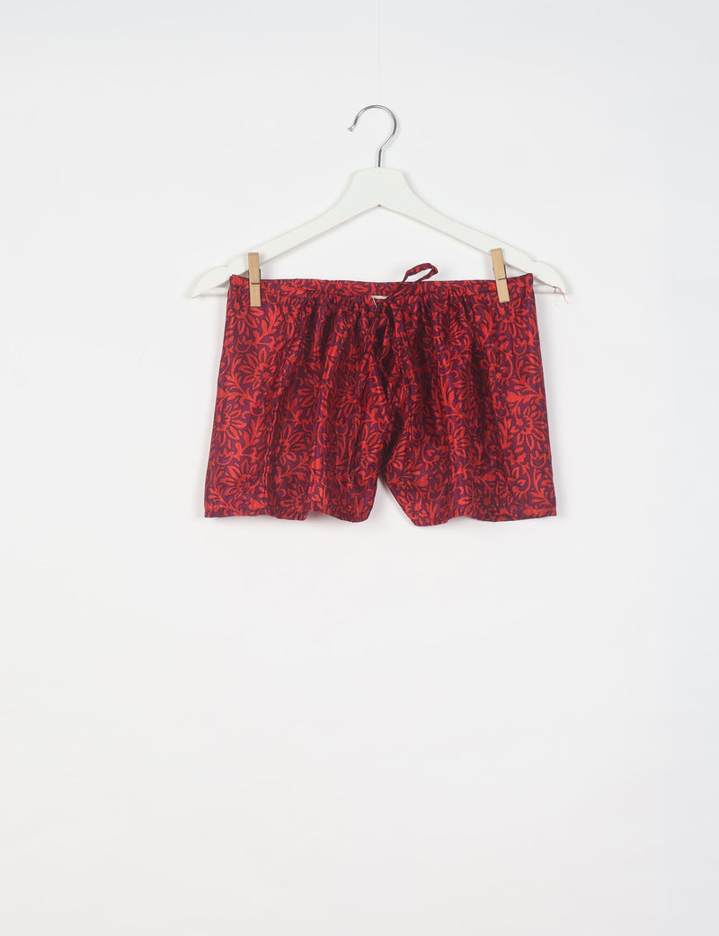 Red tropical print shorts with elastic waistband and drawstring, hanging on a white hanger against a white background