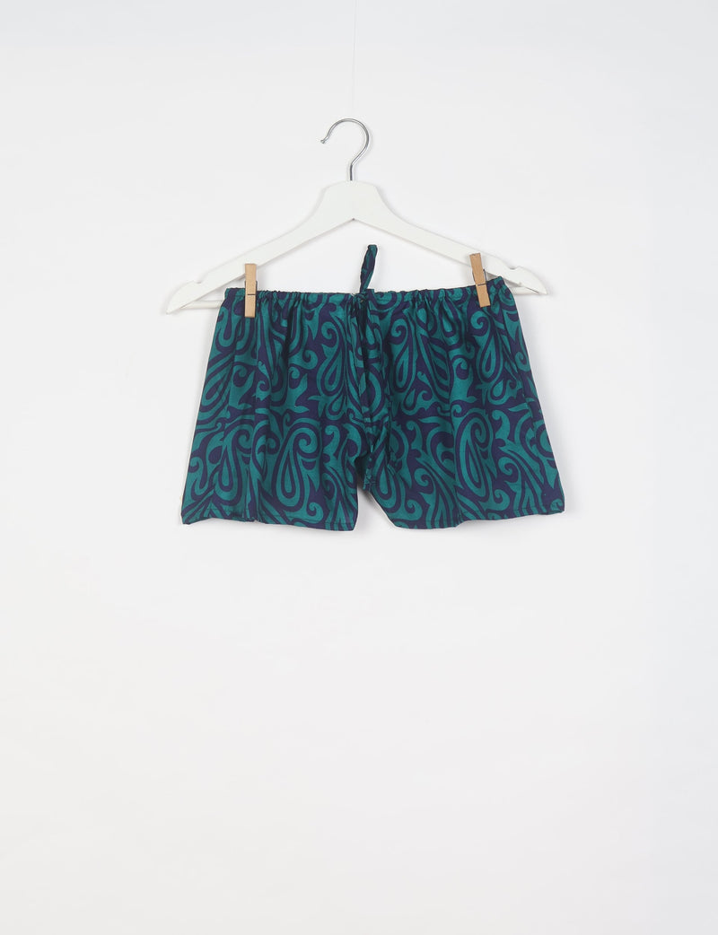 Blue and teal paisley patterned shorts with elastic waistband and drawstring, hanging on white hanger against white background