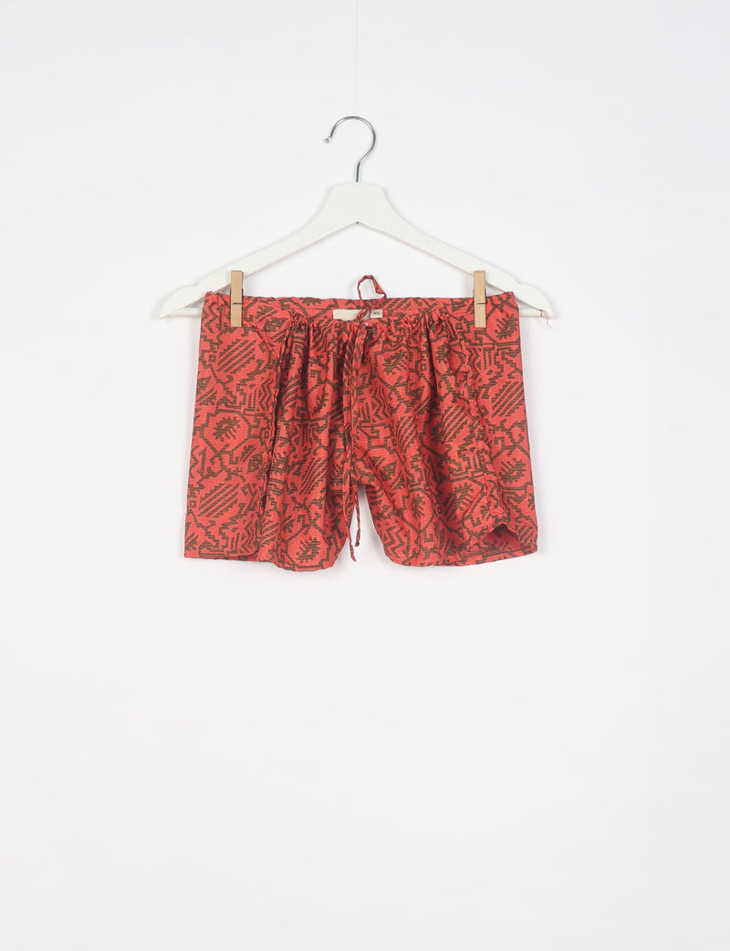 Orange shorts with dark brown tropical geometric print, elastic waistband with drawstring, hanging on white hanger front