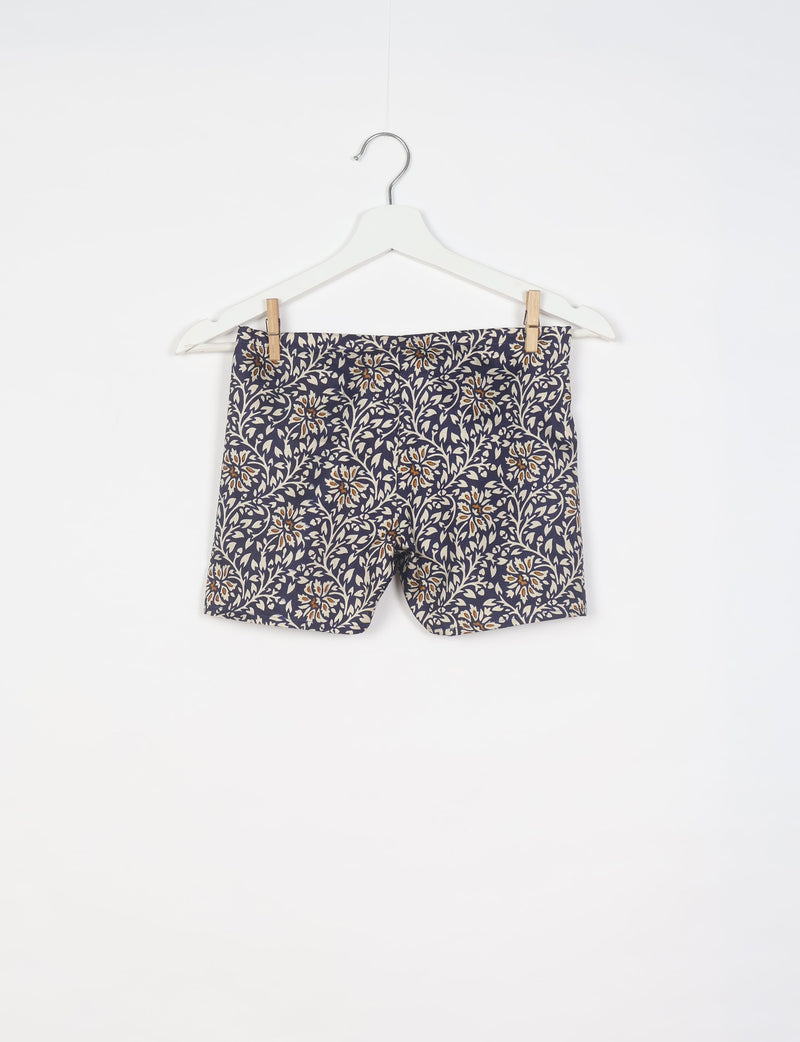 Black shorts with beige and brown tropical floral print hanging on a white hanger against a white background