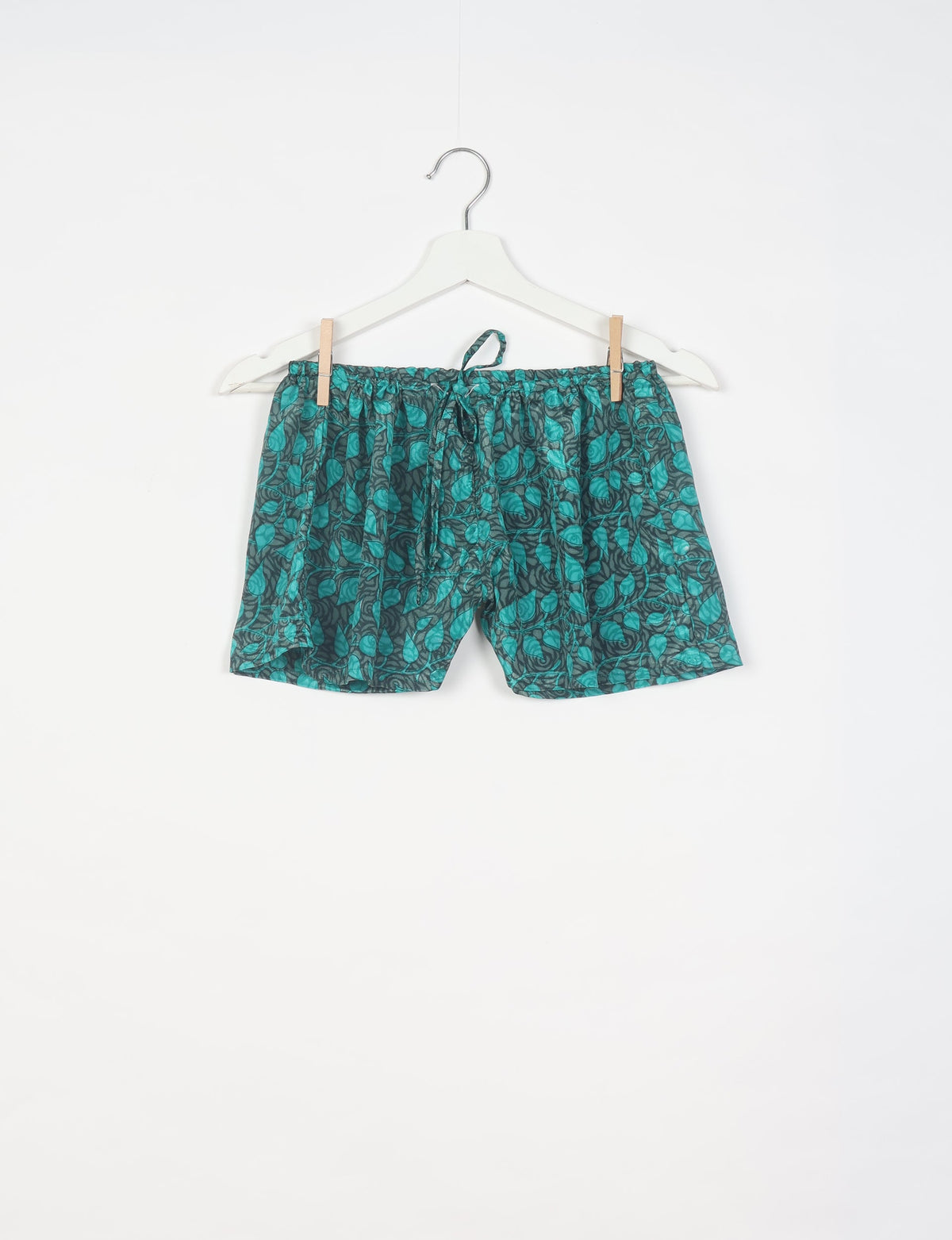 Green and black leaf-patterned shorts with elastic waistband and drawstring, hanging on white hanger against white background