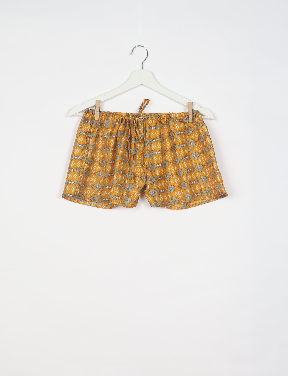 Yellow shorts with gray and white geometric pattern, elastic waistband with drawstring, hanging on white hanger