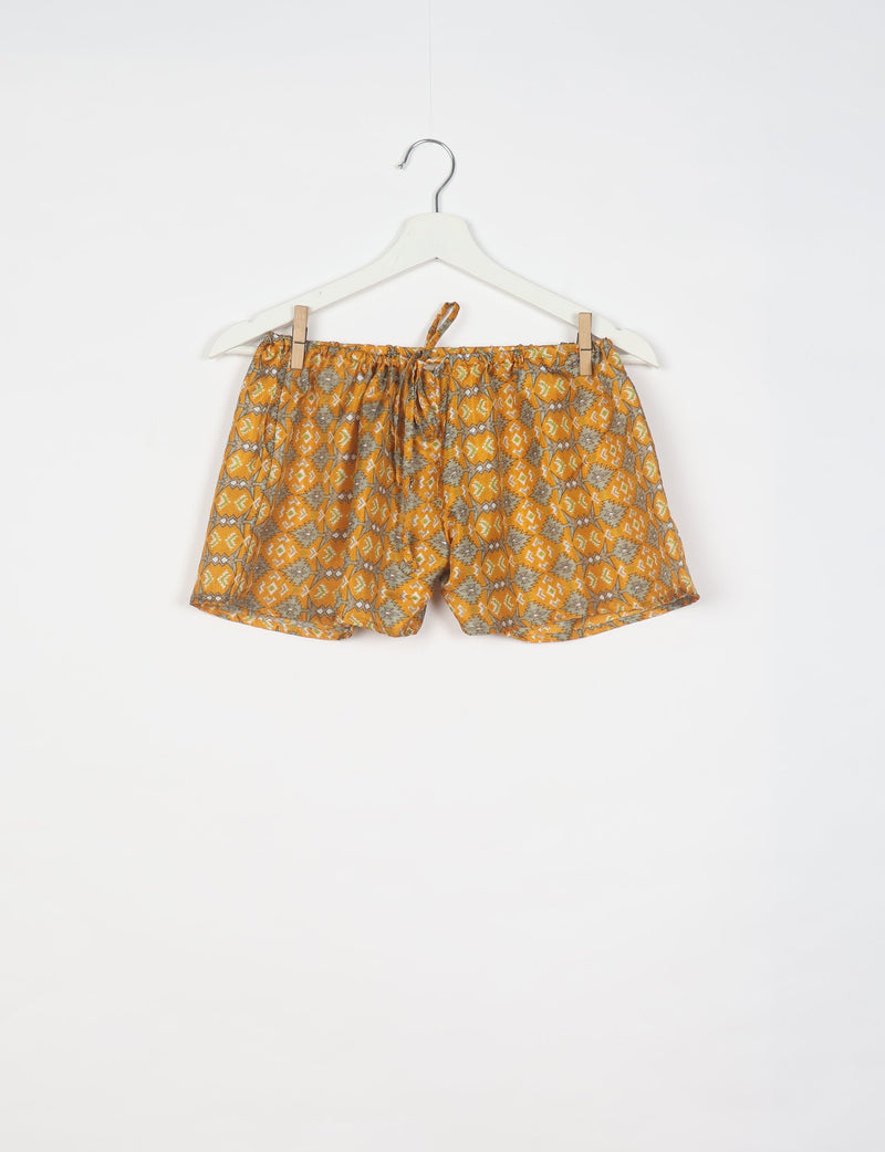 Yellow shorts with gray and white geometric pattern, elastic waistband with drawstring, hanging on white hanger