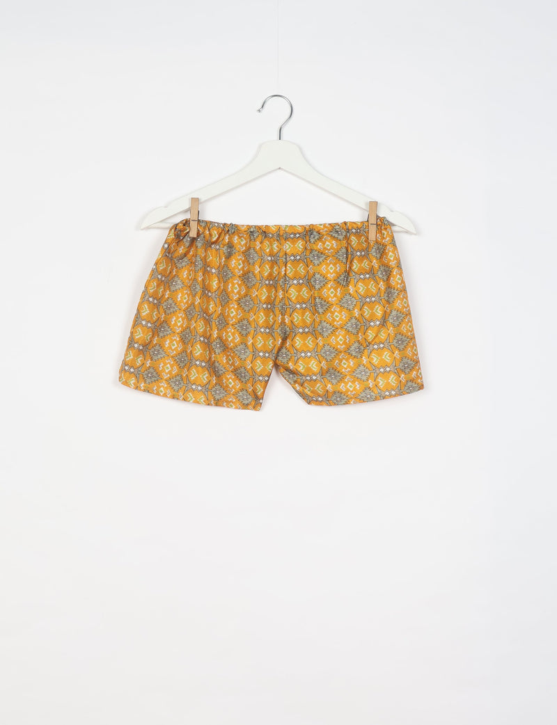 Yellow shorts with gray and white geometric pattern hanging on white hanger against white background