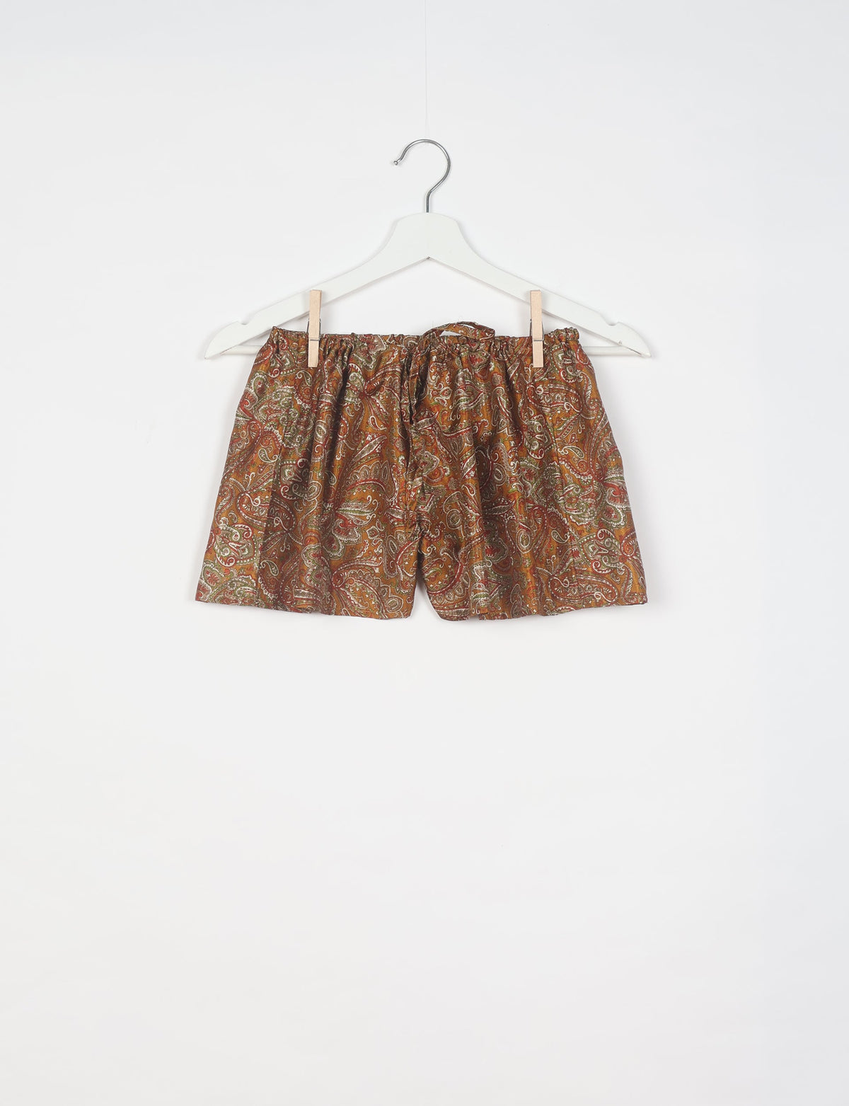 Brown paisley patterned shorts with elastic waistband and drawstring, hanging on white hanger against white background