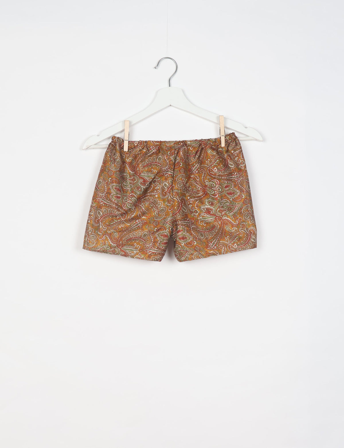 Brown paisley patterned shorts with elastic waistband hanging on white hanger against white background