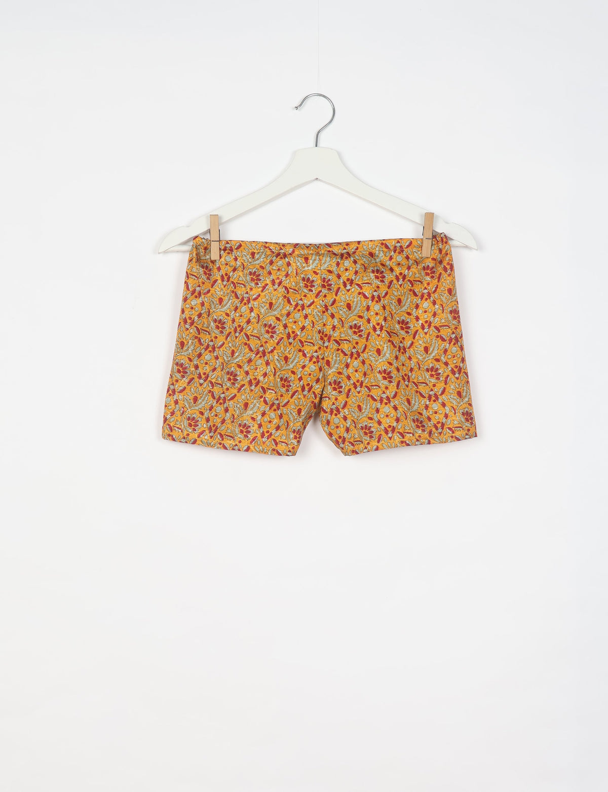 Yellow shorts with red and gray tropical floral pattern hanging on white hanger against white background