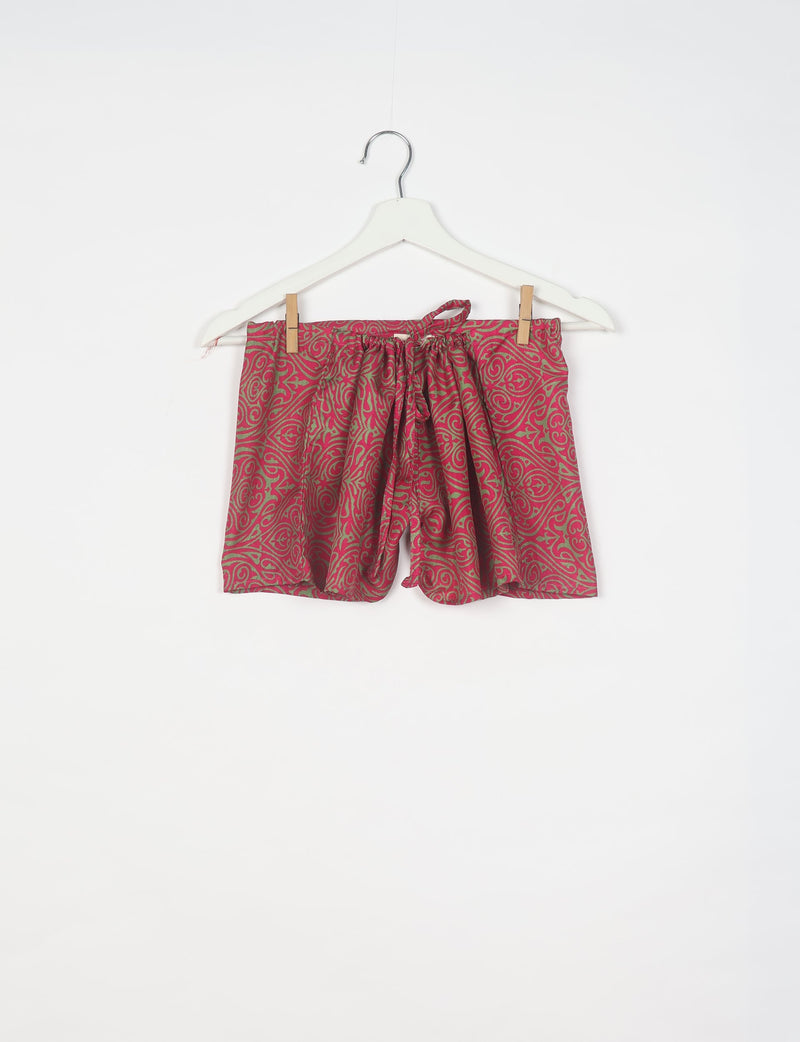 Pink shorts with green abstract swirl pattern, elastic waistband with drawstring, hanging on white hanger with clips
