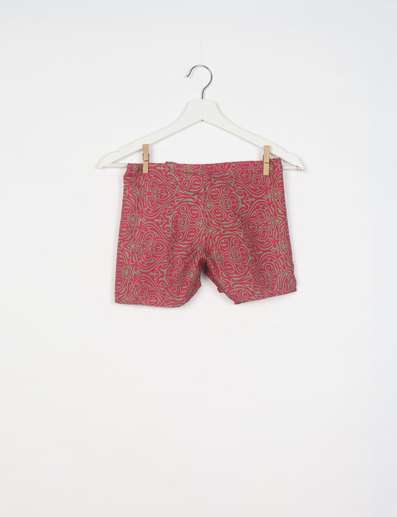 Pink shorts with green abstract swirl pattern hanging on white hanger against white background