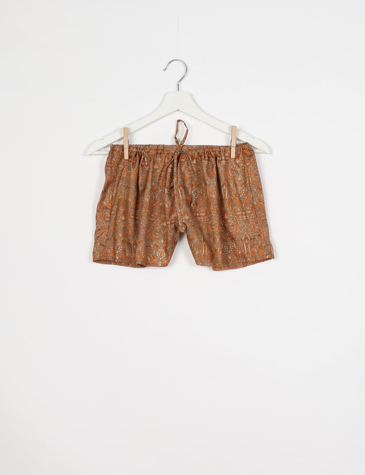 Brown and orange paisley patterned shorts with elastic waistband and drawstring, hanging on white hanger against white background