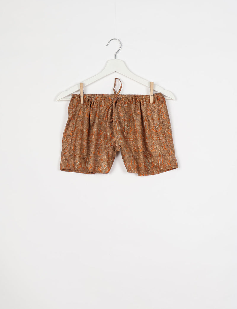 Brown and orange paisley patterned shorts with elastic waistband and drawstring, hanging on white hanger against white background