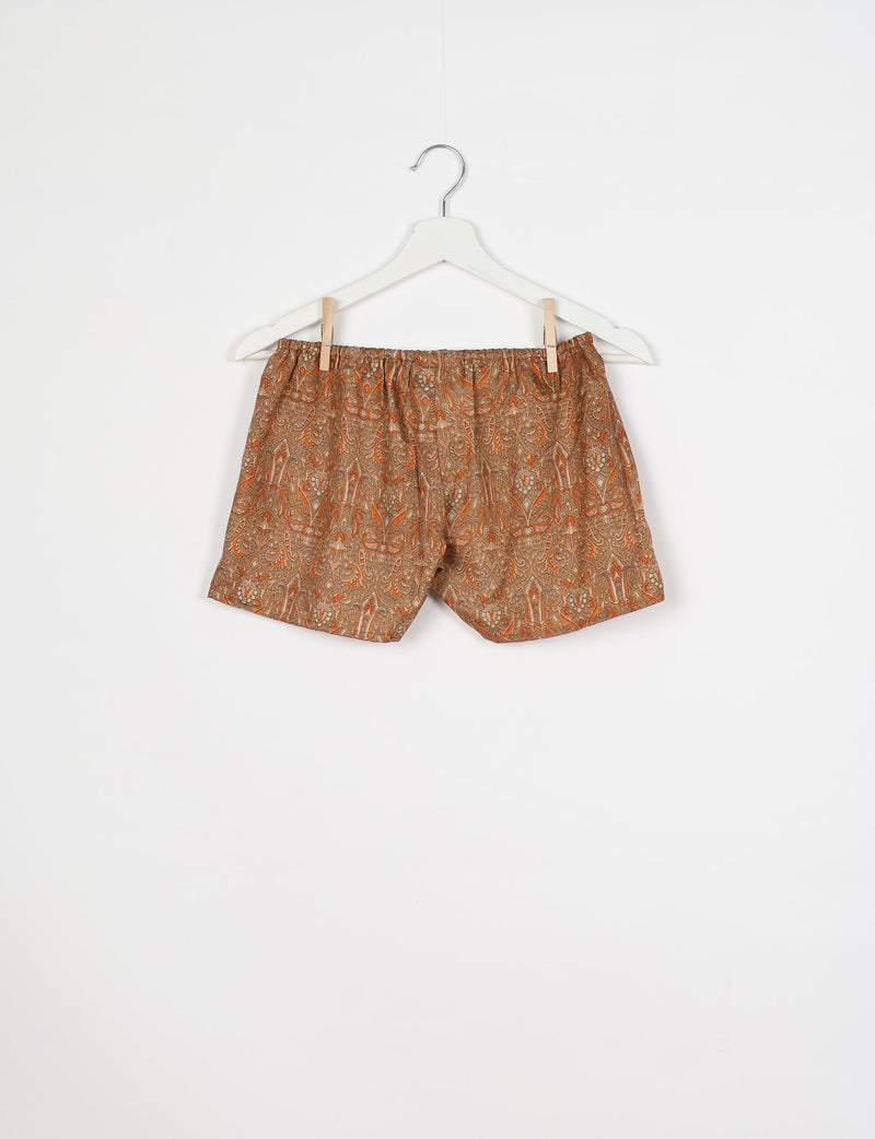 Brown and orange paisley patterned shorts with elastic waistband hanging on white hanger against white background