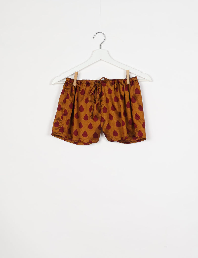 Yellow shorts with maroon teardrop pattern, elastic waistband with drawstring, hanging on white hanger against white background