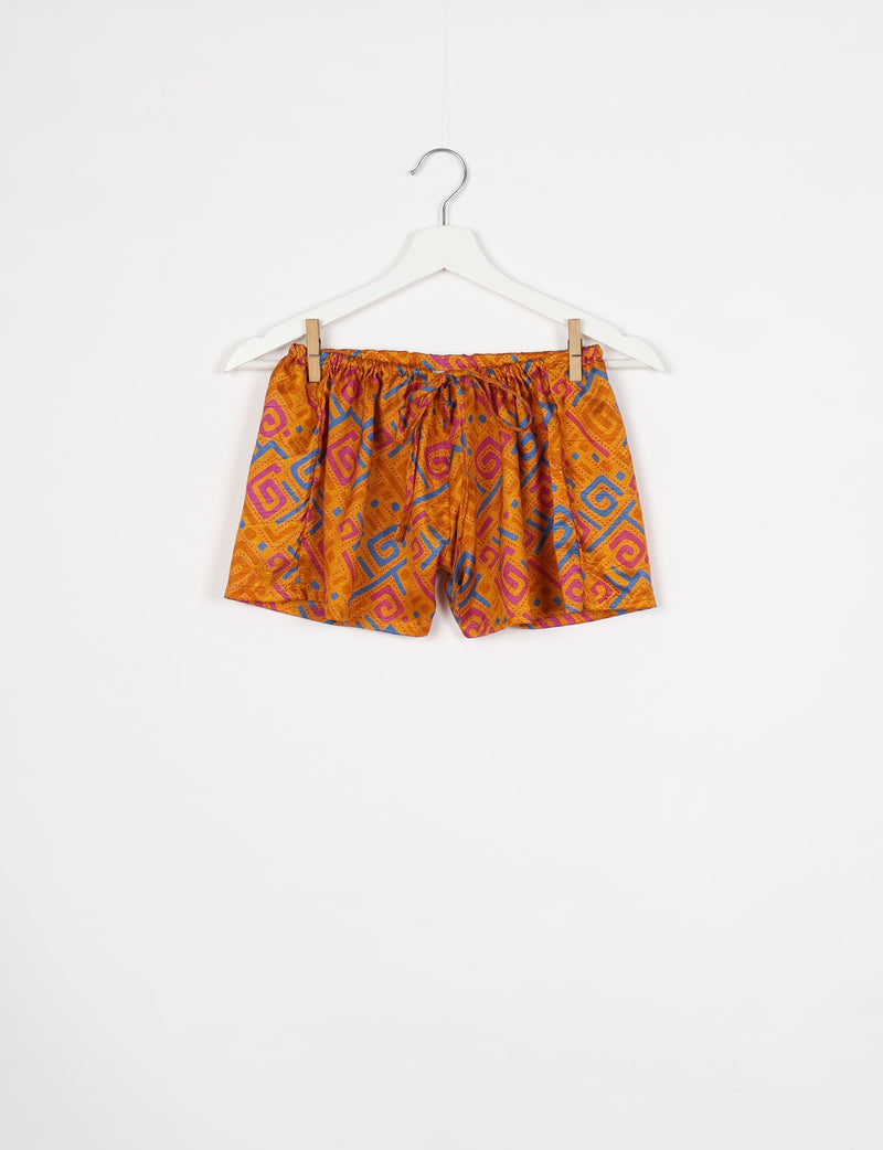 Yellow shorts with abstract pink and blue geometric patterns, elastic waistband, and drawstring, hanging on white hanger