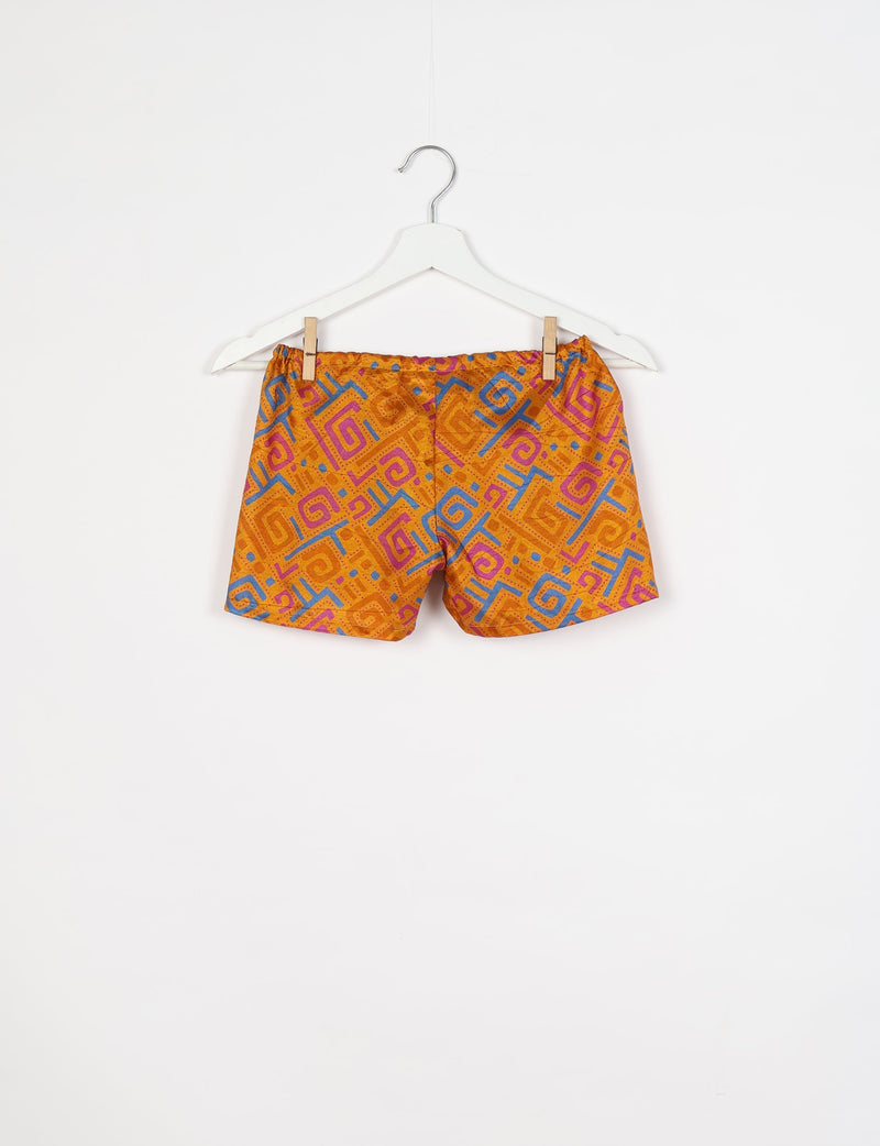 Yellow shorts with abstract pink and blue geometric patterns hanging on a white hanger against a white background