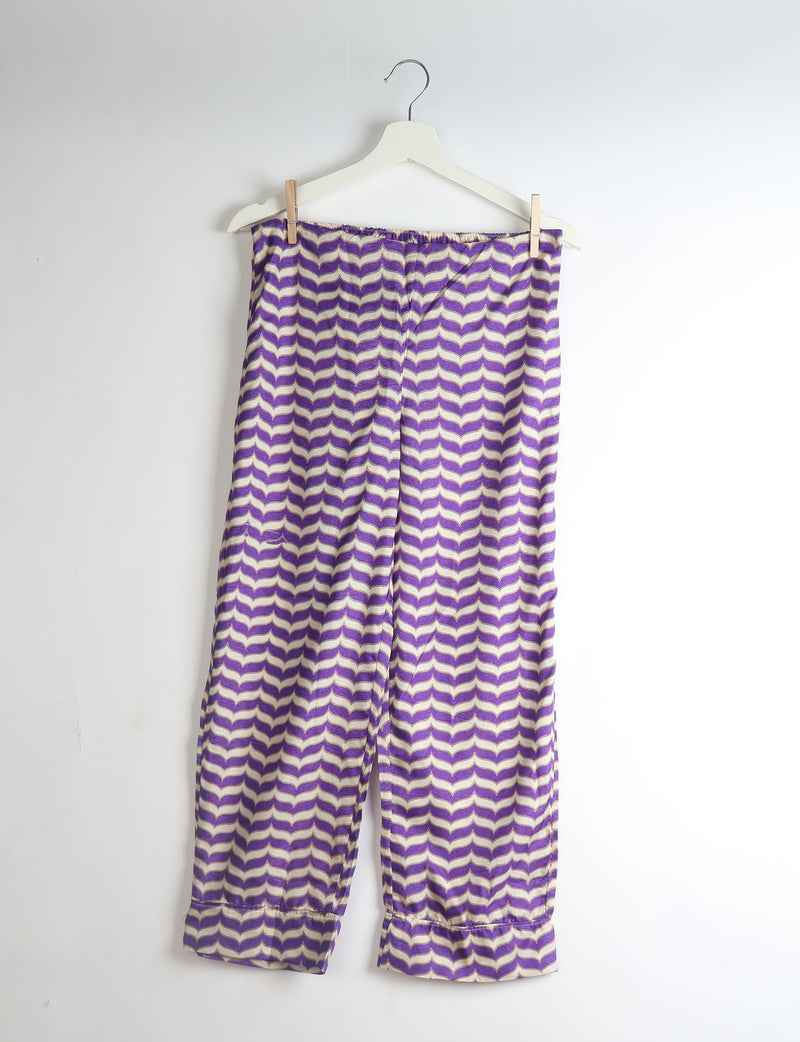 Purple and beige abstract patterned pajama pants with elastic waistband and ruffled cuffs hanging on white hanger
