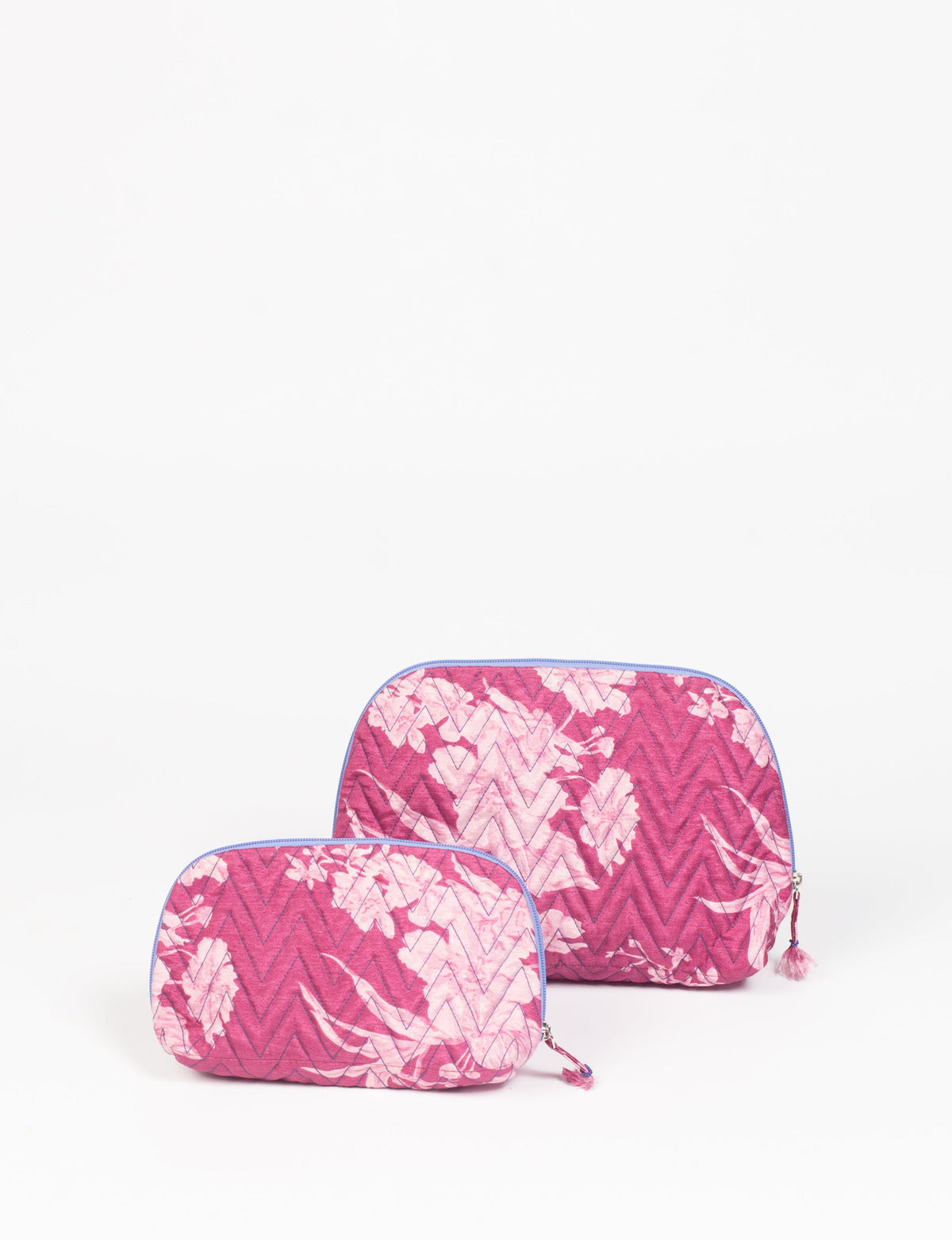 Set of two pink tropical patterned quilted vanity pouches with blue zipper and tassel pull, front view on white background