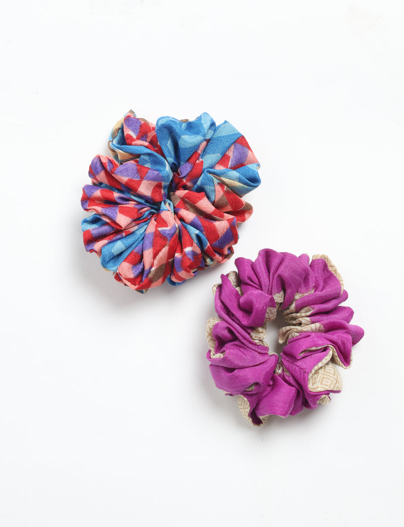 Set of two scrunchies, one with blue, red, purple abstract pattern and one purple with beige geometric accents, flat lay view