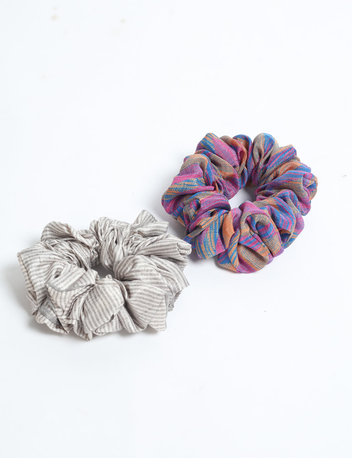 Set of two scrunchies, one with gray and white stripes and one with multicolor pink, blue, and orange pattern, flat lay