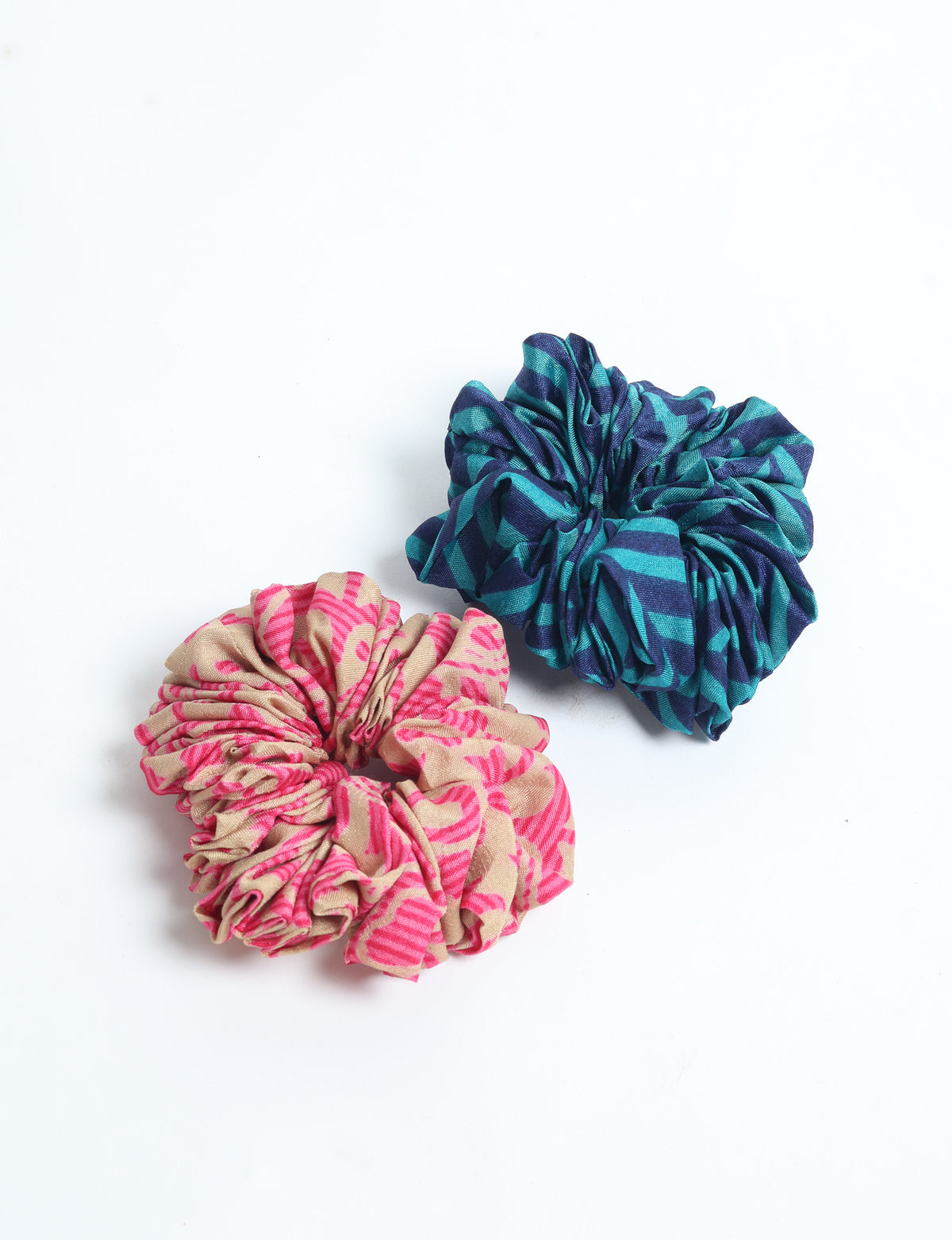Set of two fabric scrunchies, one beige with pink floral pattern and one blue with teal striped pattern, flat lay view