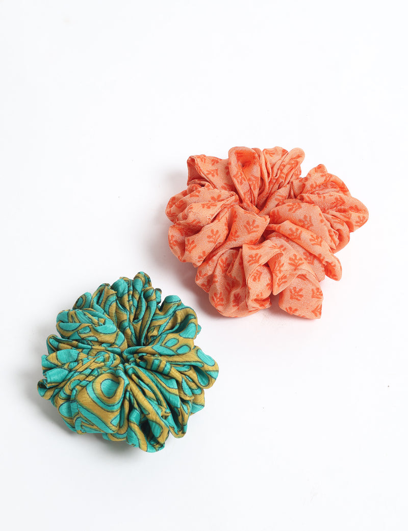 Set of two fabric scrunchies, one orange with small floral print and one teal with abstract yellow pattern, flat lay on white