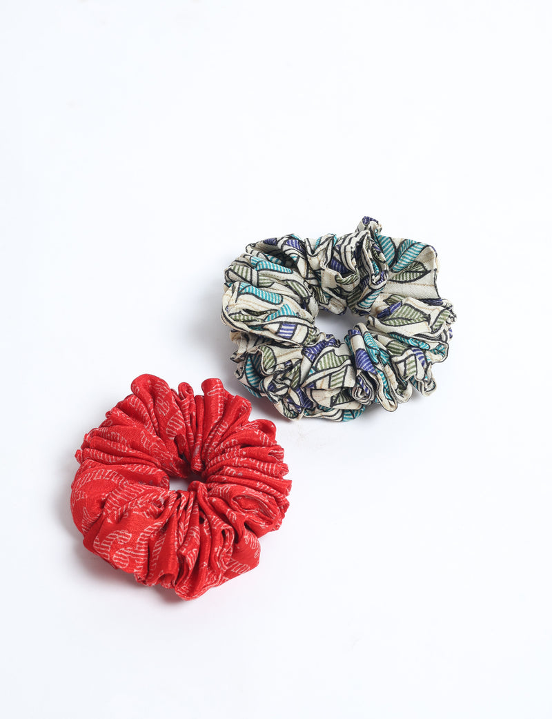Set of two assorted scrunchies, one red with white pattern and one beige with blue and green leaf print, flat lay on white background