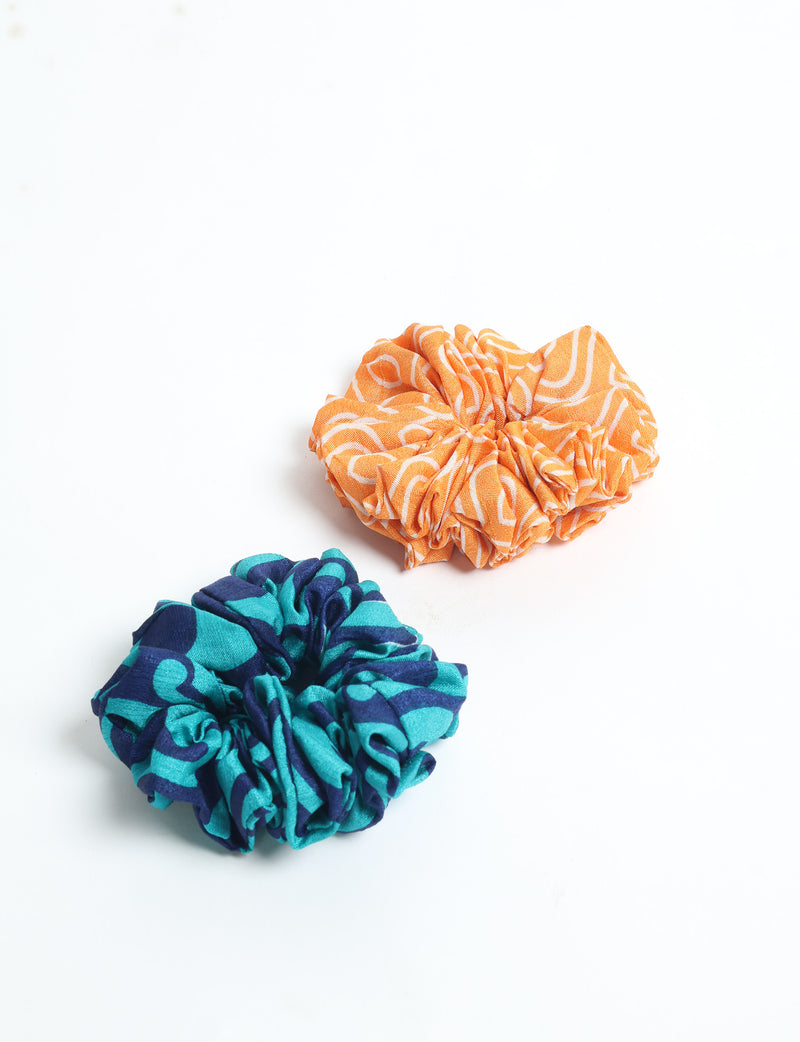 Set of two assorted scrunchies, one orange with white pattern and one blue with teal pattern, flat lay on white background