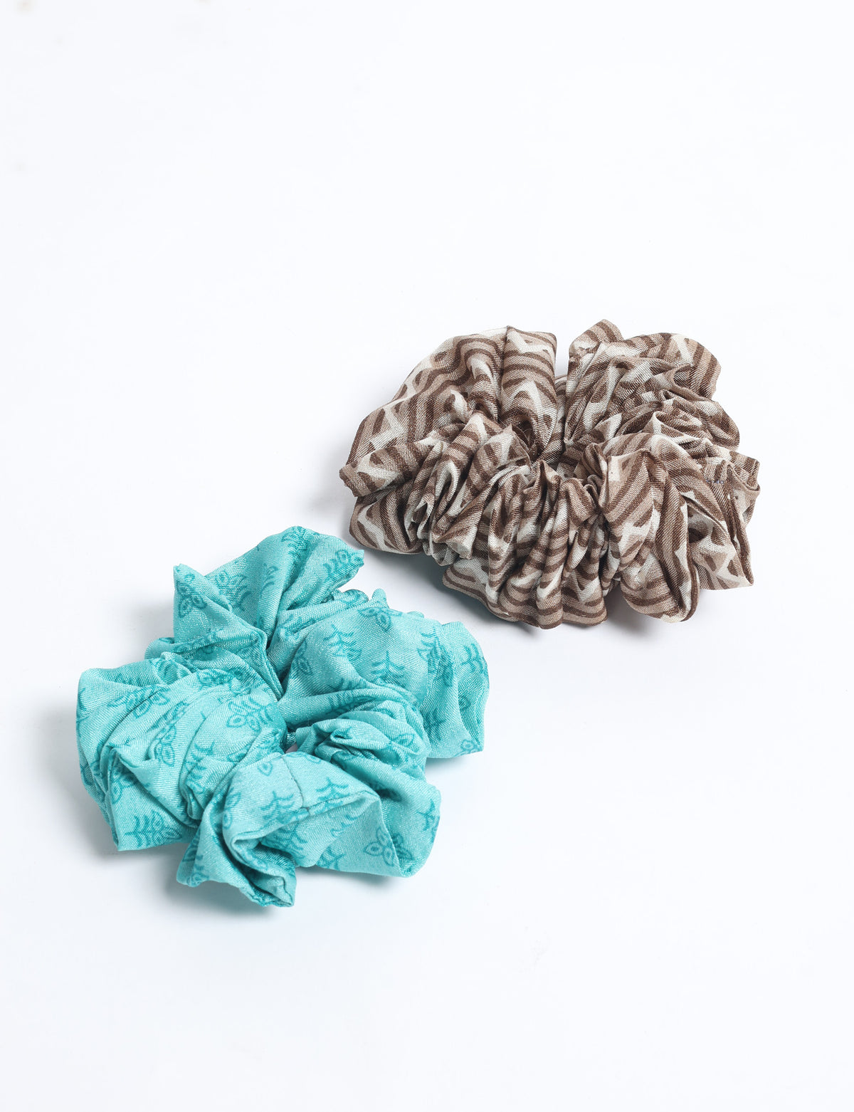 Set of two scrunchies, one light blue with leaf pattern and one brown with abstract stripes, flat lay on white background
