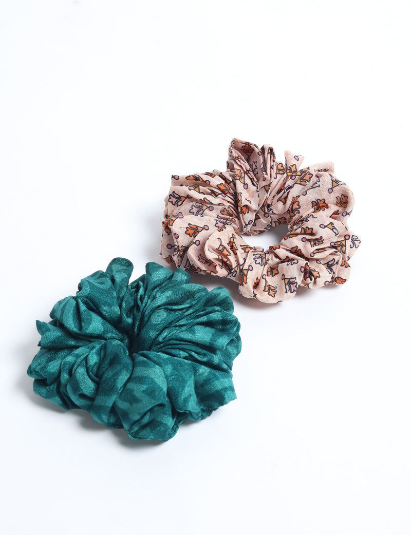 Set of 2 scrunchies, one teal solid and one beige with orange and pink floral print, flat lay on white background