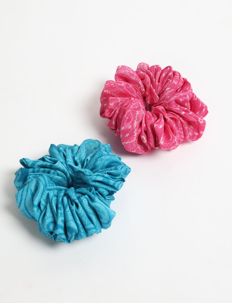 Set of two fabric scrunchies in pink and blue with subtle white patterns, shown flat on a white background