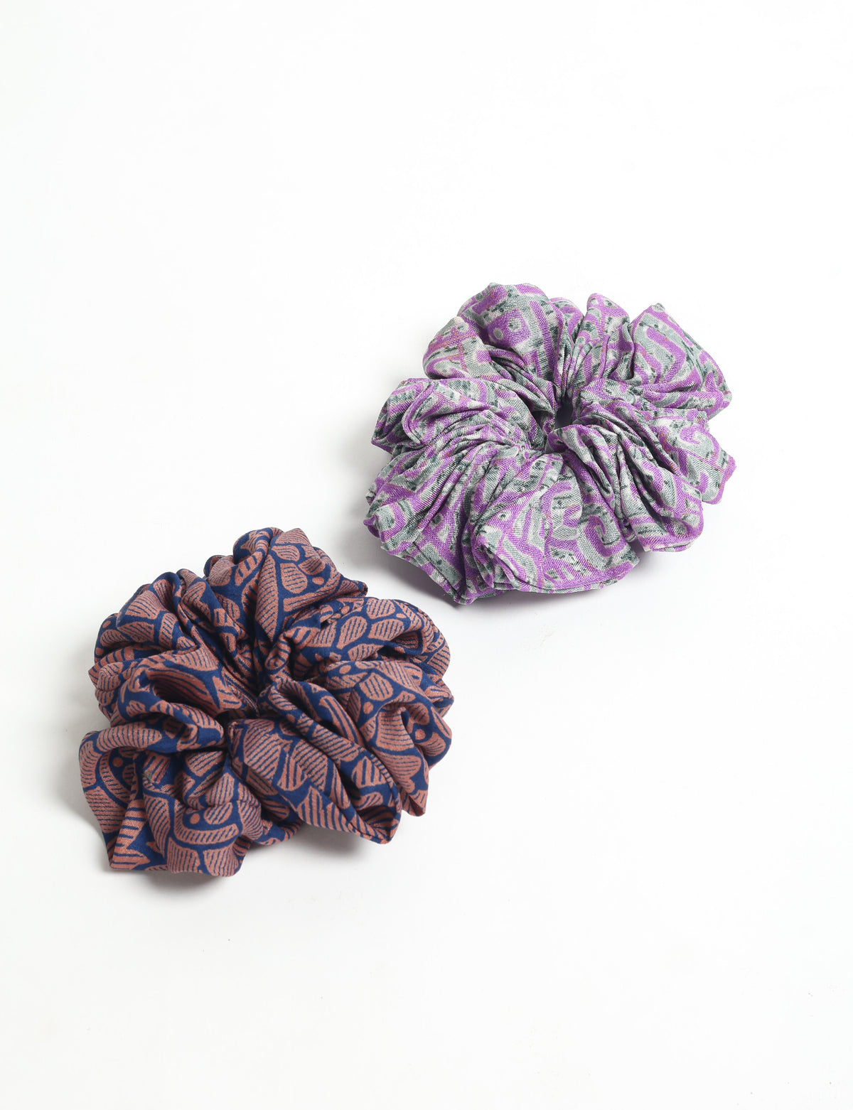 Set of two fabric scrunchies with abstract patterns, one purple and gray, the other navy blue and brown, flat lay view