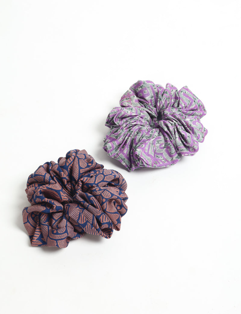 Set of two fabric scrunchies with abstract patterns, one purple and gray, the other navy blue and brown, flat lay view