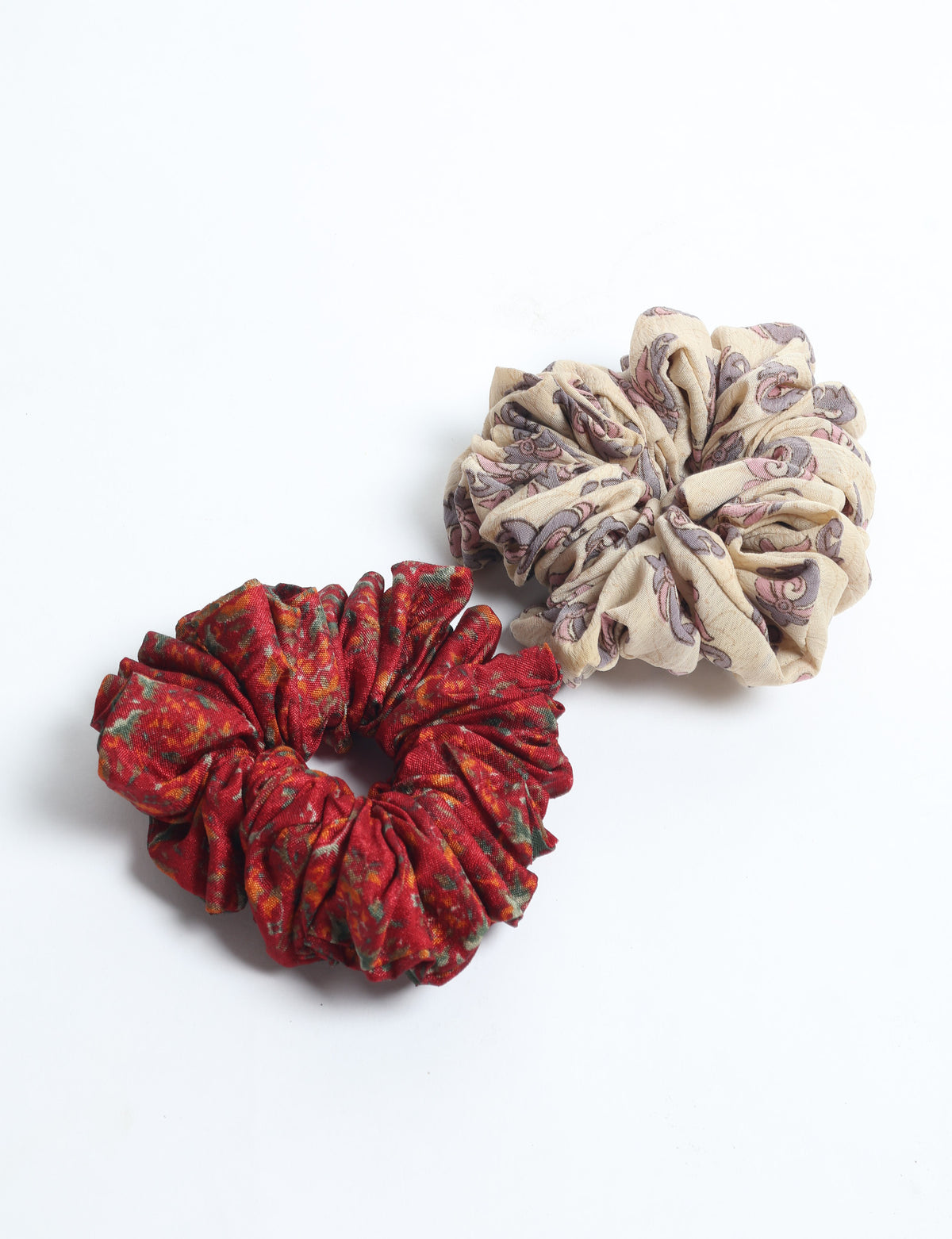 Set of two fabric scrunchies, one beige with purple and pink paisley pattern, one red with multicolor floral pattern, flat