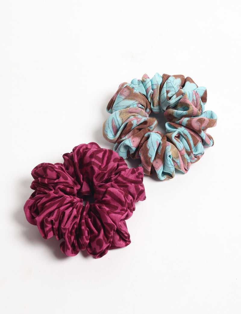 Set of two scrunchies, one with blue, brown, and pink floral pattern, and one solid dark pink with subtle pattern, flat lay