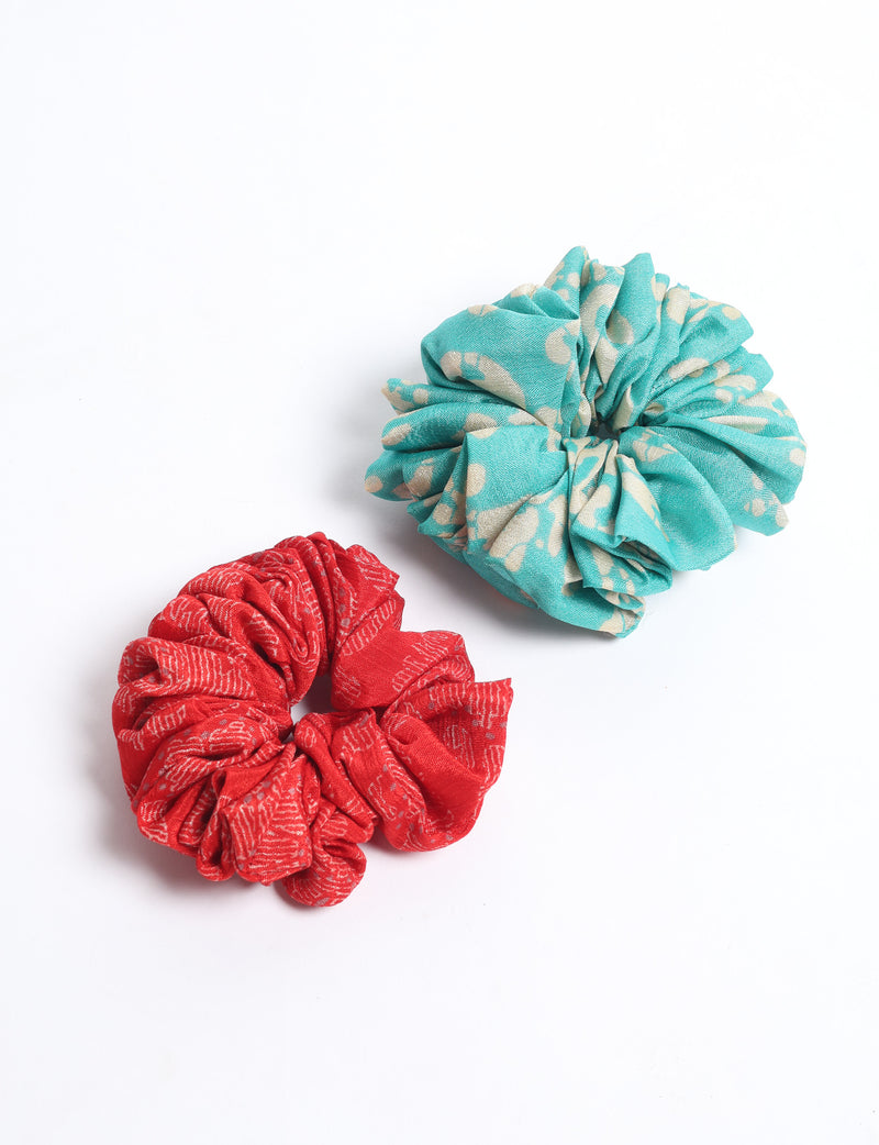Set of two fabric scrunchies, one turquoise with beige abstract spots, one red with white linear pattern, flat lay on white