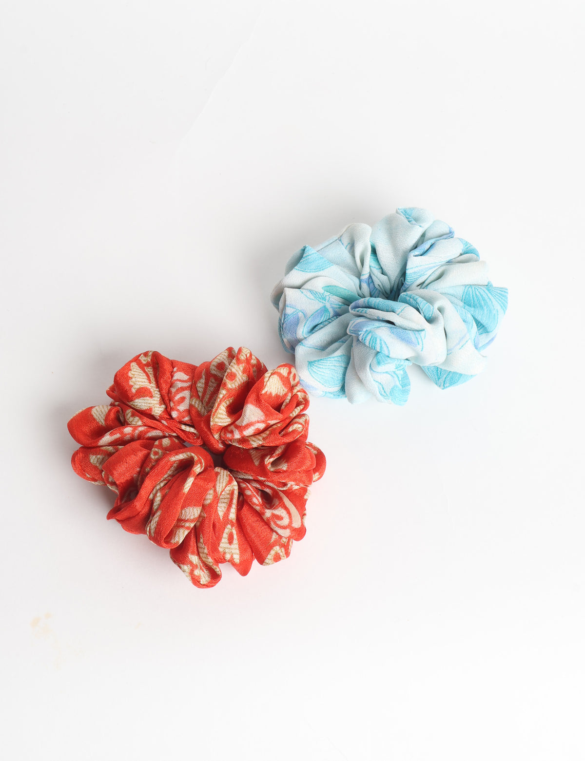 Set of two fabric scrunchies, one turquoise with beige abstract spots, one red with white linear pattern, flat lay on white