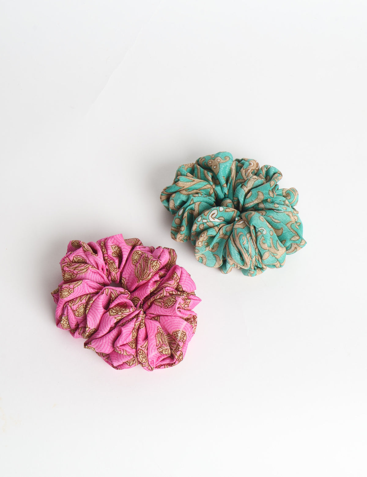 Set of two fabric scrunchies, one turquoise with beige abstract spots, one red with white linear pattern, flat lay on white