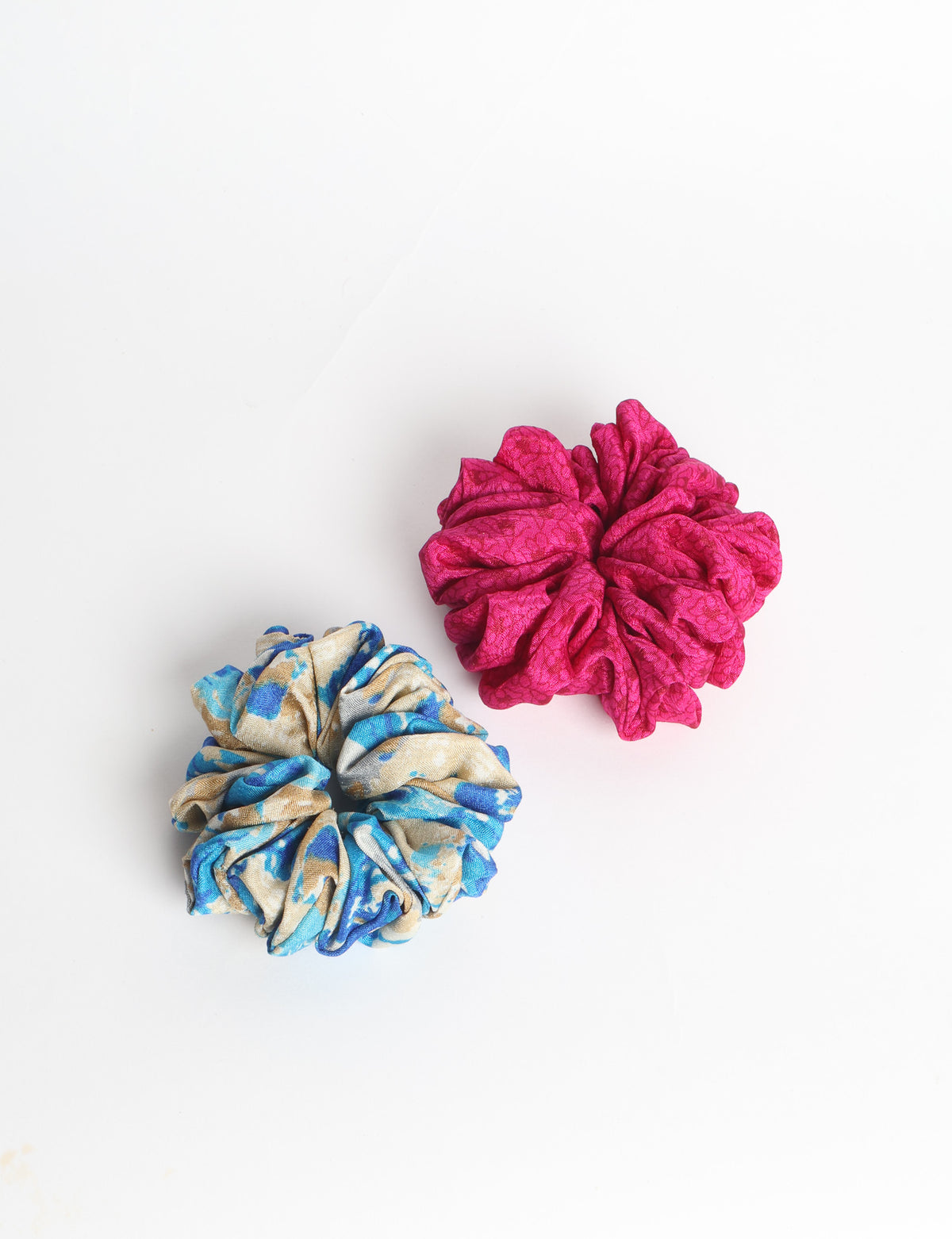 Set of two fabric scrunchies, one turquoise with beige abstract spots, one red with white linear pattern, flat lay on white