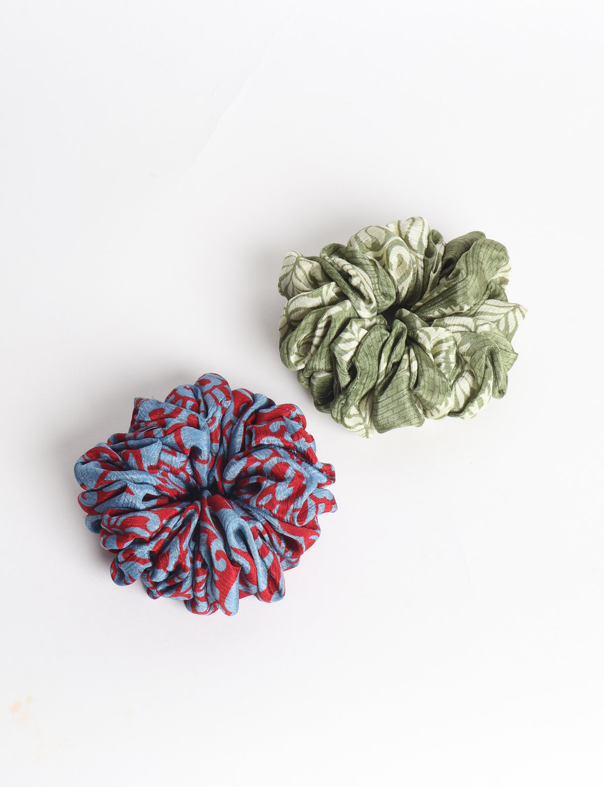 Set of two fabric scrunchies, one turquoise with beige abstract spots, one red with white linear pattern, flat lay on white
