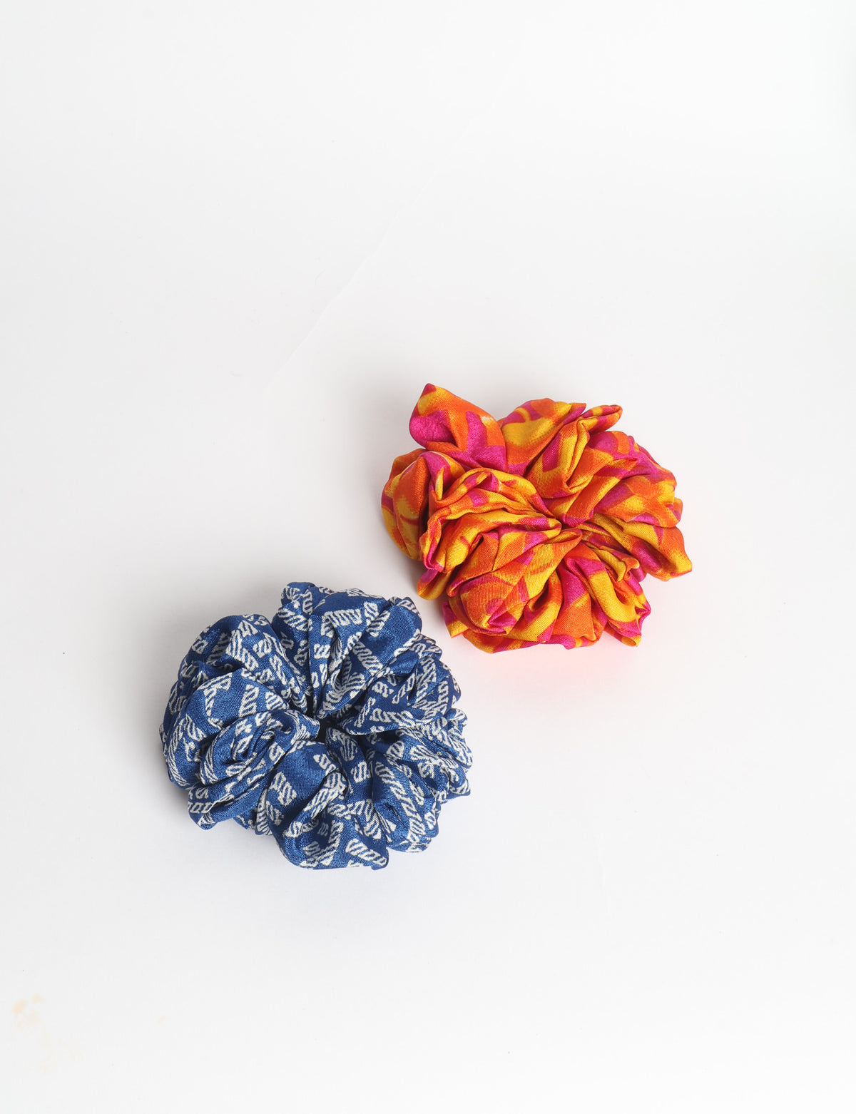 Set of two fabric scrunchies, one turquoise with beige abstract spots, one red with white linear pattern, flat lay on white