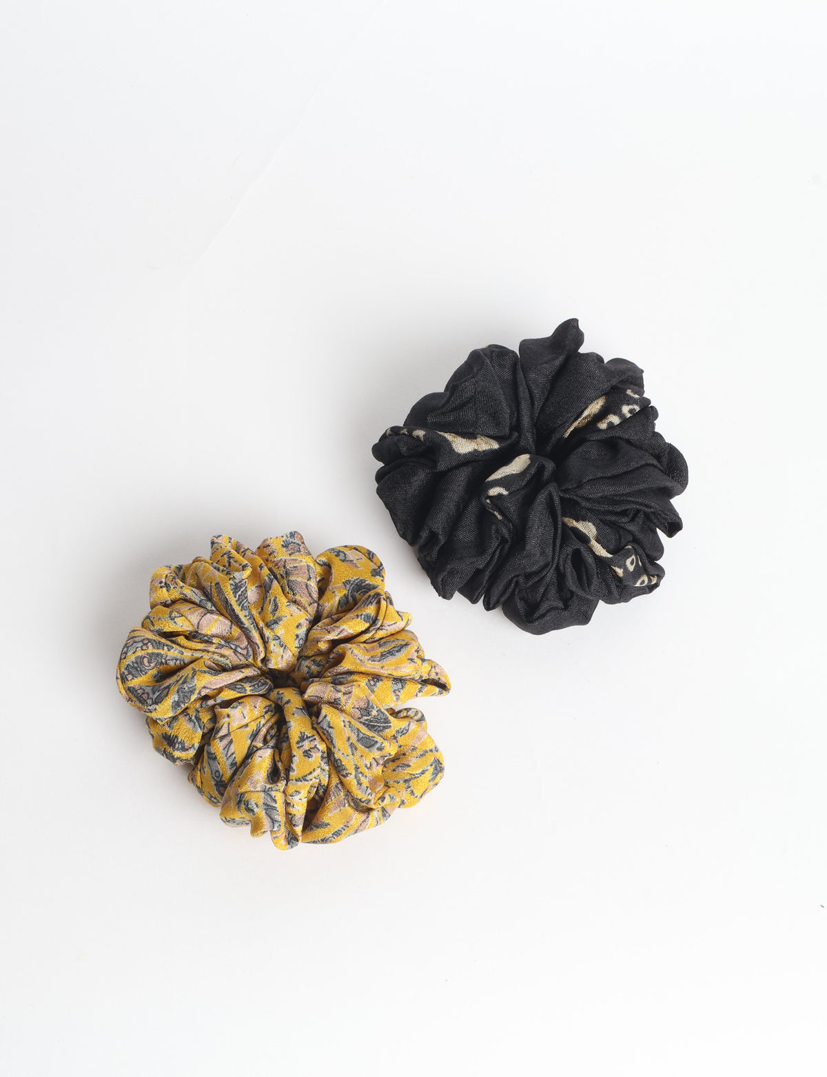 Set of two fabric scrunchies, one turquoise with beige abstract spots, one red with white linear pattern, flat lay on white