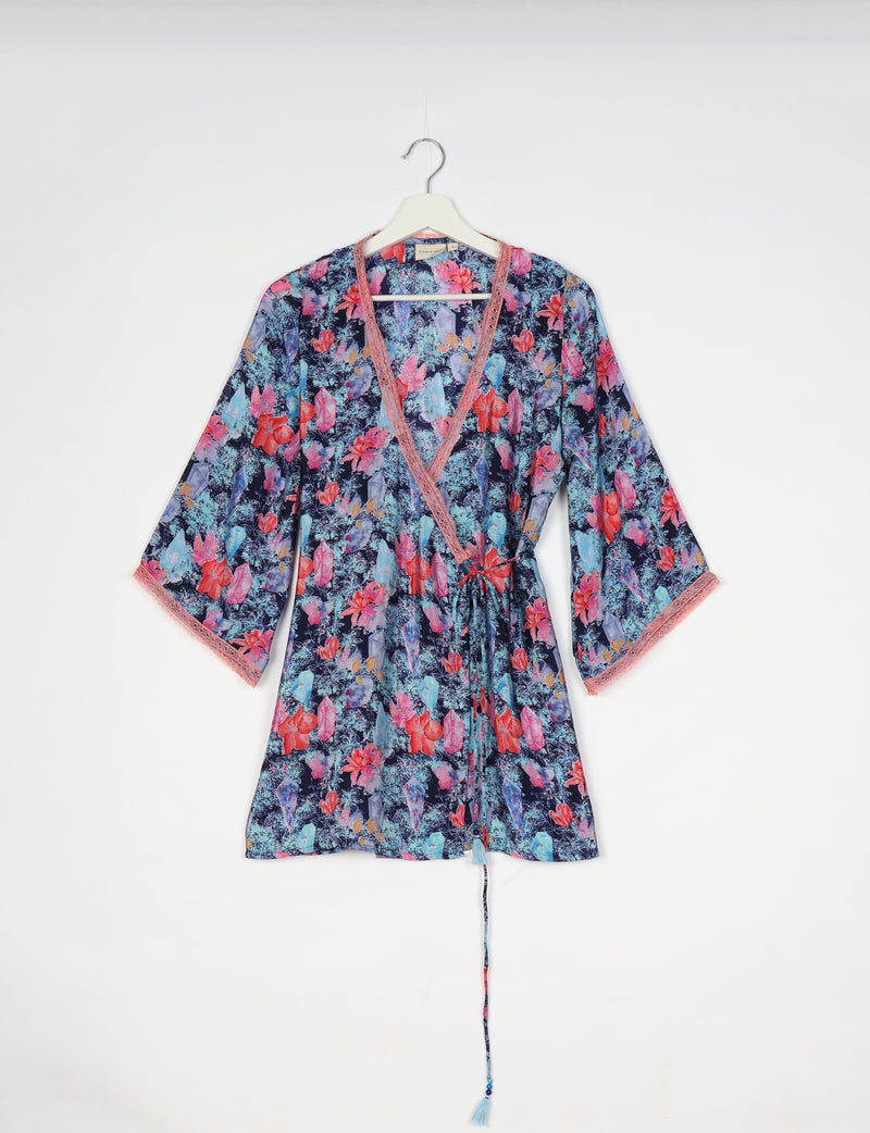 Blue floral tunic with pink lace trim, long sleeves, and a front tie, hanging on a white hanger