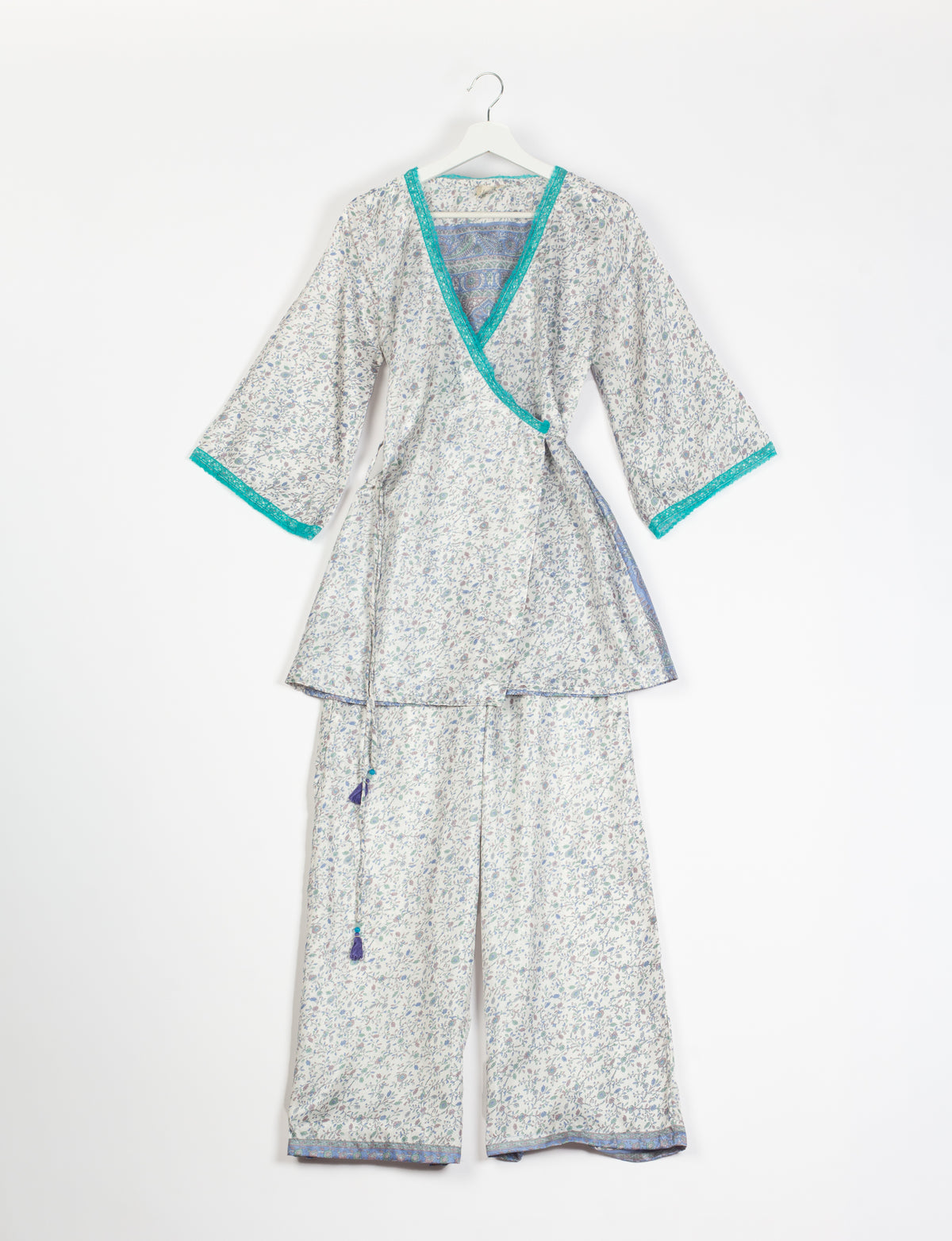Grey floral print tunic set with turquoise trim on neckline and sleeves, wide-leg pants, and wrap-style top on hanger