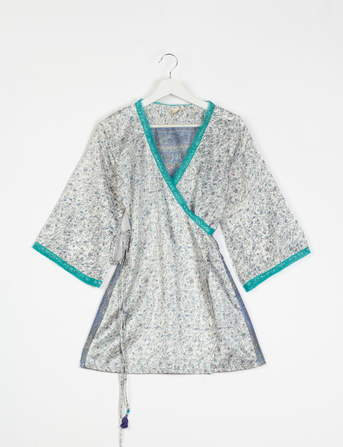 Grey floral print tunic with teal lace trim on neckline and sleeves, wrap style with side tie, hanging on white hanger