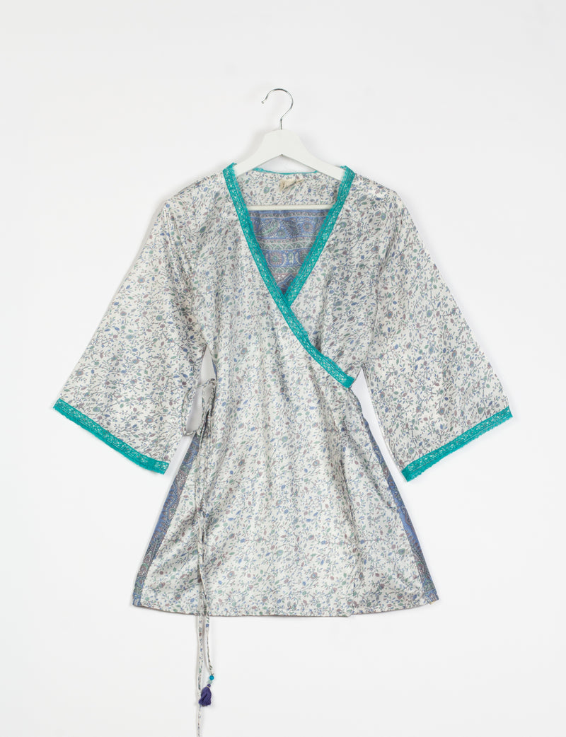 Grey floral print tunic with teal lace trim on neckline and sleeves, wrap style with side tie, hanging on white hanger