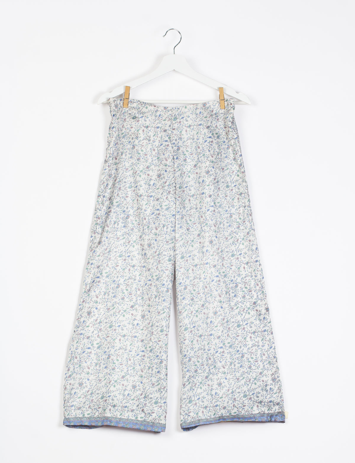 White wide-leg pants with small blue and green floral print and blue patterned trim at hem, hanging on white hanger