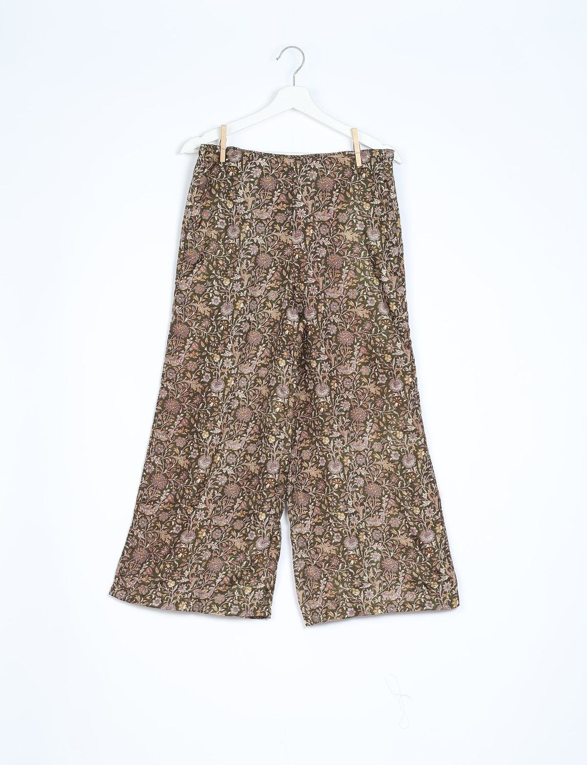 Brown tropical floral patterned wide-leg pants hanging on white hanger against white background