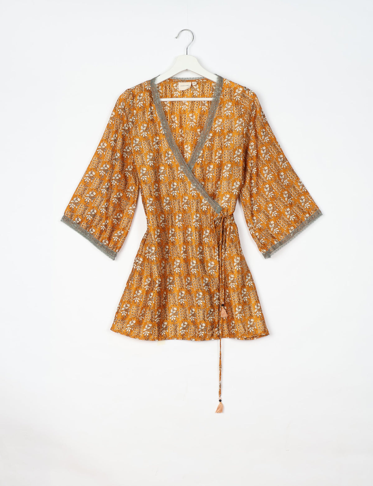 Yellow-orange floral wrap tunic with gray lace trim on neckline and sleeves, hanging on white hanger against white background