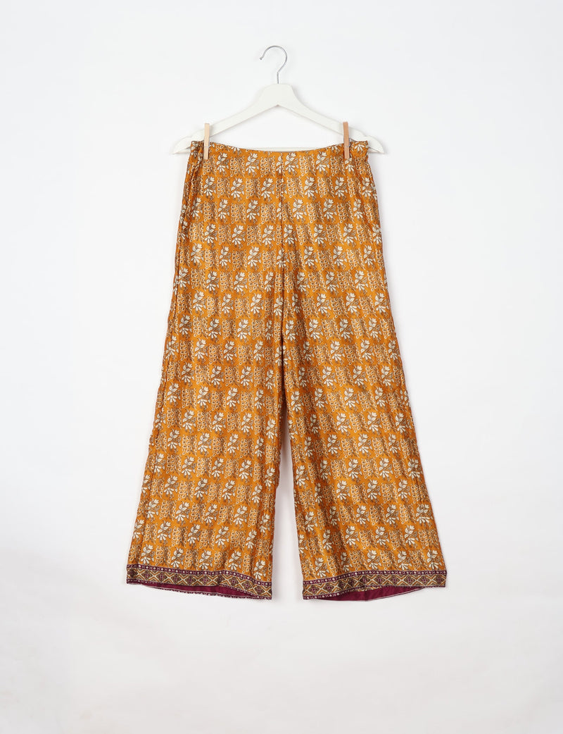 Yellow tropical print wide-leg pants with elastic waistband and maroon patterned hem, hanging on white hanger