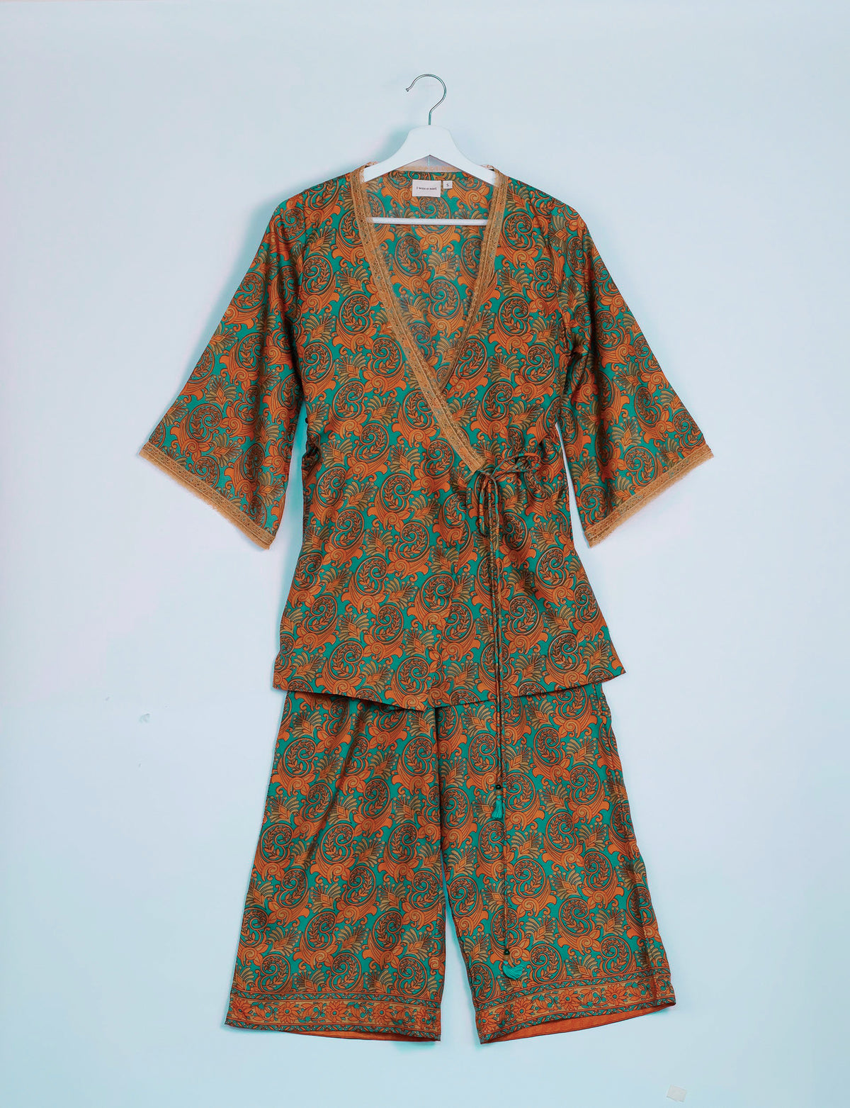 Green paisley print tunic set with wrap top, lace trim, and matching shorts hanging on white hanger against light background